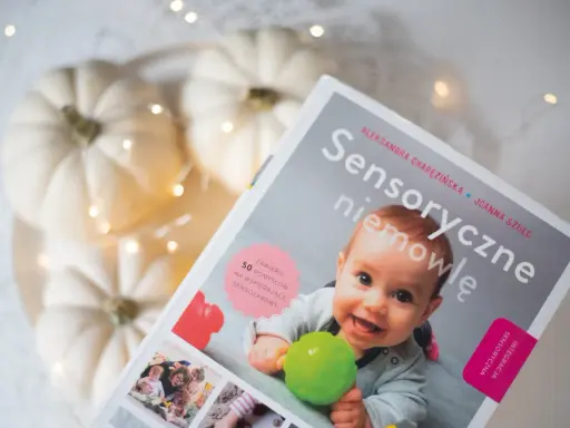 Okładka książki "Sensoryczne niemowlę" z uśmiechniętym dzieckiem, dyniami i lampkami.